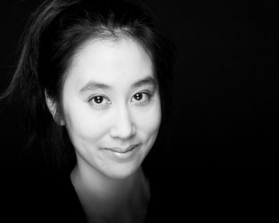 A black and white picture of a young female presenting asian-canadian person, looking straight at the camera and slightly smiling.