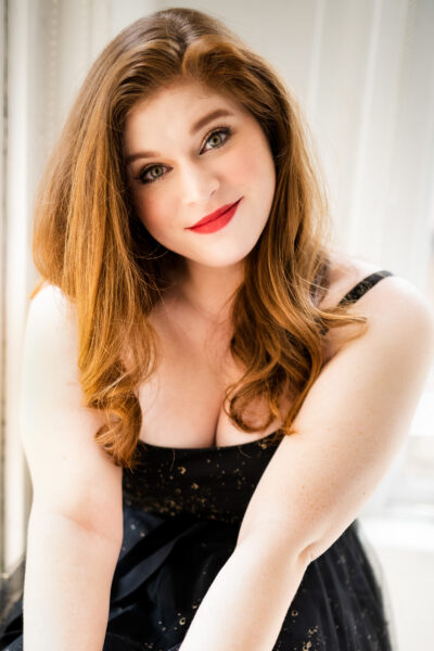 Photo of a red-haired woman in a black tank-top dress smiling.